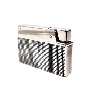 May include: A silver-toned lighter with a rectangular shape. The top is hinged and the lower portion features a black and white grid pattern. The lighter has a shiny, metallic finish and is set against a white background.