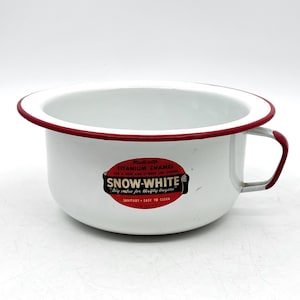 May include: White enamelware chamber pot with a red rim and handle. The pot has a rounded shape and features the text "SNOW-WHITE" on a red and black label. The text also reads "SANITARY - EASY TO CLEAN".
