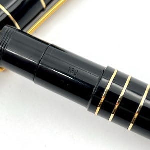 Puede incluir: Primer plano de una pluma estilogr&aacute;fica negra con detalles dorados. El bol&iacute;grafo tiene un acabado brillante y bandas doradas. El n&uacute;mero "133" es visible en el cuerpo del bol&iacute;grafo.