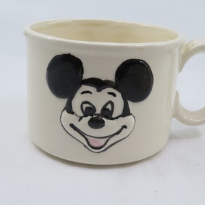 May include: White ceramic mug with a black and white image of Mickey Mouse's face.