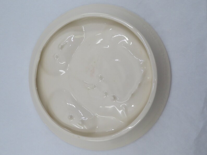 May include: White ceramic plate with a raised, textured design on the bottom. The plate has a smooth, glossy finish.