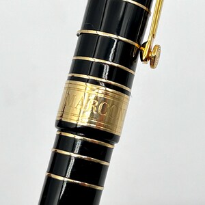 Puede incluir: Primer plano de un bol&iacute;grafo MARCON negro y dorado. El bol&iacute;grafo tiene un cuerpo negro brillante con detalles y adornos dorados. La palabra "MARCON" est&aacute; grabada en una banda dorada. El clip y el plum&iacute;n del bol&iacute;grafo tambi&eacute;n son dorados.