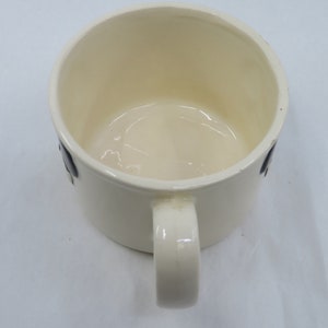 May include: White ceramic mug with a black handle and a black design on the side.