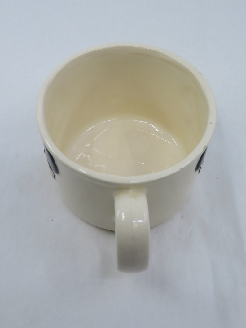 May include: White ceramic mug with a black handle and a black design on the side.