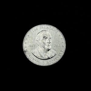 May include: A silver coin featuring a portrait of Franklin D. Roosevelt, the 32nd President of the United States. The coin is inscribed with "32nd PRESIDENT", "1933", and "1945", along with the name "FRANKLIN D ROOSEVELT". The coin has a detailed design and is set against a black background.