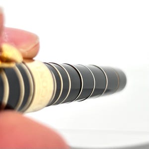 Puede incluir: Primer plano de un bol&iacute;grafo negro y dorado con una serie de bandas negras y doradas. El bol&iacute;grafo tiene un dise&ntilde;o elegante y moderno con un acabado brillante. El bol&iacute;grafo est&aacute; sostenido por los dedos de una persona.