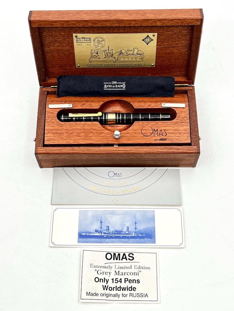 Puede incluir: Un juego de pluma de lujo en una caja de madera. La pluma es negra y dorada, con la marca "OMAS" visible. La caja incluye una placa conmemorativa y un certificado. El juego es una edici&oacute;n limitada, "Grey Marconi", con solo 154 plumas en todo el mundo.