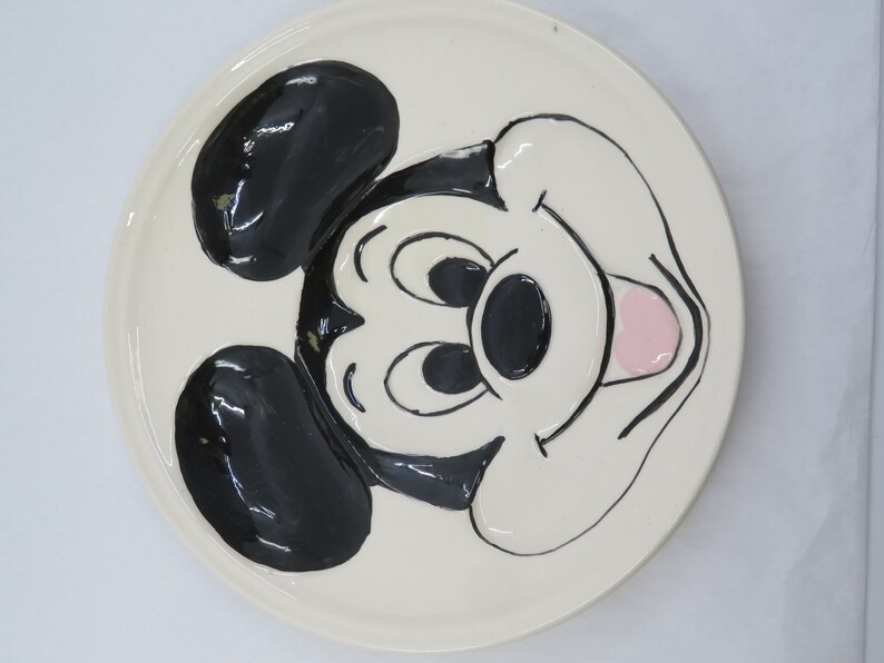 May include: White ceramic plate with a black and white cartoon image of Mickey Mouse. Mickey Mouse is smiling with his tongue sticking out.