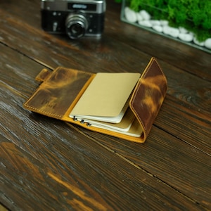 Peut inclure: Journal en cuir ouvert avec une finition jaune-brun vieillie. Le journal contient plusieurs blocs-notes vierges avec une reliure à spirale. Le mot "Mark" est estampé sur la couverture. Un appareil photo vintage est en arrière-plan.