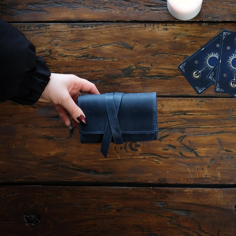Pode incluir: Uma bolsa retangular de couro azul-marinho com fecho de amarrar. A bolsa tem costuras vis&iacute;veis ao longo das bordas e um acabamento fosco liso. &Eacute; mantida na posi&ccedil;&atilde;o horizontal, exibindo sua constru&ccedil;&atilde;o e design simples.