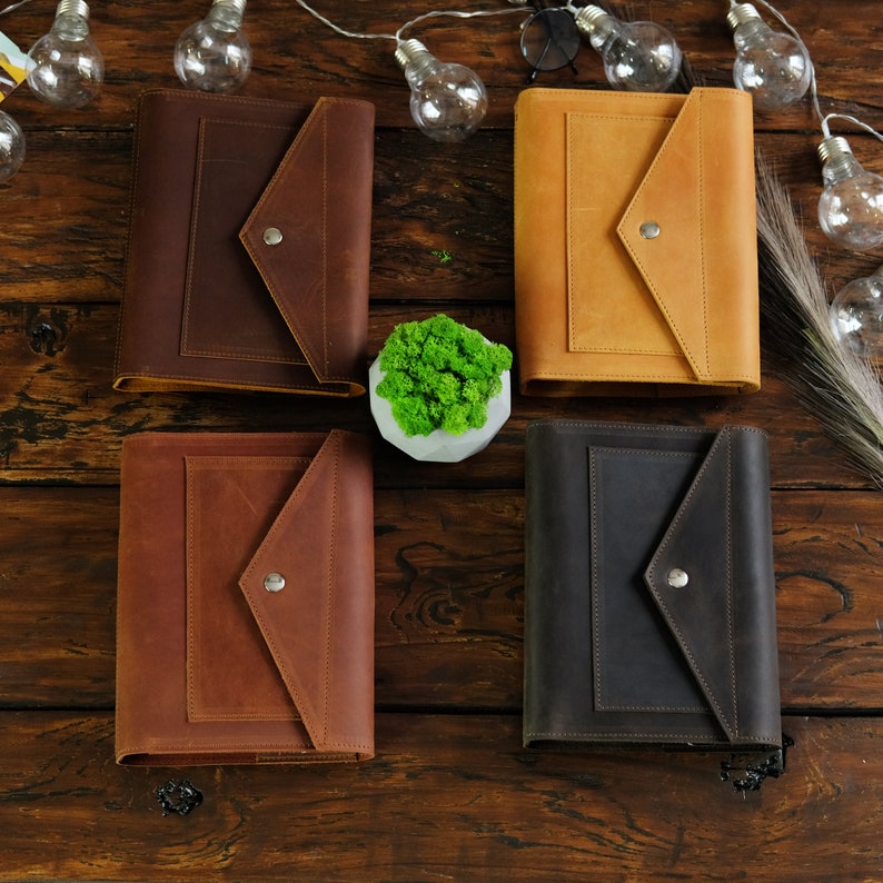 May include: Four leather-bound journals with a flap closure and a button detail. The journals are in brown, tan, and black.