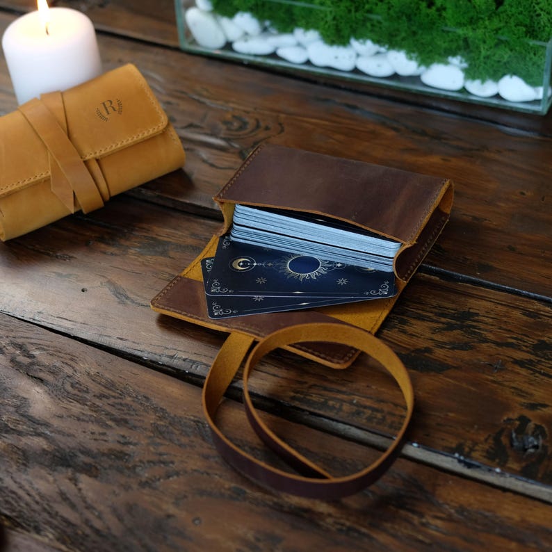 May include: A brown leather card case with a yellow leather strap. The case is open and a deck of cards is visible inside. The cards have a blue and gold design with a moon and stars.
