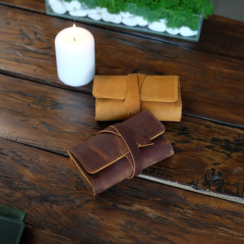 Pode incluir: Duas bolsas retangulares de couro com fechos de amarrar. Uma bolsa &eacute; de cor castanho-claro e a outra &eacute; de cor castanho-escura. Ambos os itens apresentam costuras vis&iacute;veis ao longo das bordas e um acabamento liso e fosco na superf&iacute;cie.