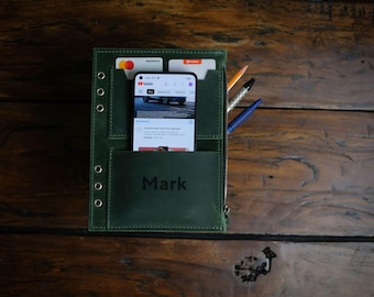 Könnte beinhalten: Ein grünes Ledernotizbuch mit Reißverschluss, einem Telefon, zwei Karten und zwei Stiften. Das Notizbuch hat eine Tasche für ein Telefon und eine Tasche für Karten. Das Notizbuch ist mit dem Namen "Mark" personalisiert.