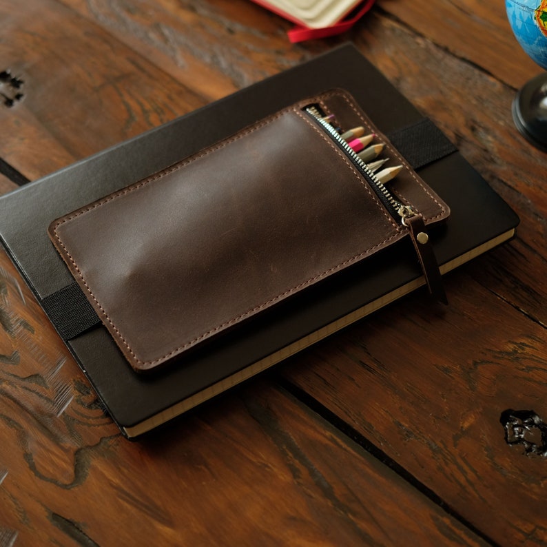 Leather pencil case with zipper. This pen pouch has a wide elastic band for putting on a notebook.
