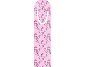 May include: A pink bookmark with a floral pattern. The design features clusters of pink flowers with green leaves and white accents, arranged in a repeating pattern. The bookmark has a curved top and a cutout for easy placement in a book.