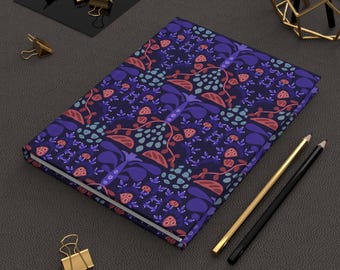 May include: A rectangular notebook featuring a dark blue cover with a repeating pattern of stylized purple, light blue, and reddish-orange floral and leaf shapes. The notebook is positioned next to a gold-colored pencil and a black pencil.