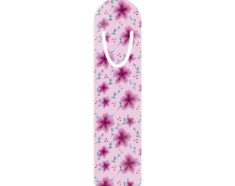 May include: A floral bookmark with a light pink background. The bookmark features a repeating pattern of purple flowers, small blue leaves, and tiny red dots. A white loop is at the top for easy use.