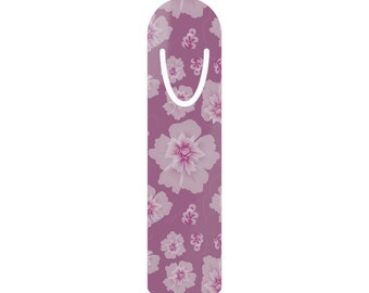 May include: A floral bookmark with a purple background and white and pink flower pattern. The bookmark has a rounded top with a white curved cutout for easy placement in a book. The flowers vary in size and are evenly distributed.