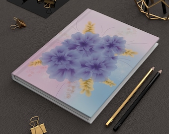 May include: A hardcover notebook featuring a soft gradient background transitioning from light pink to blue, decorated with a central cluster of purple flowers and small yellow sprigs. The notebook is accompanied by a gold pen and a black pen.