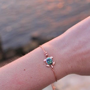 May include: A rose gold chain bracelet with a small green and blue turtle charm.