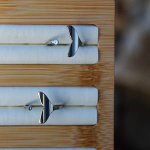 May include: Two silver rings with a mermaid tail design are displayed on a wooden jewellery organiser. The rings are adjustable and feature a small, round detail on the band. The mermaid tail is the focal point.