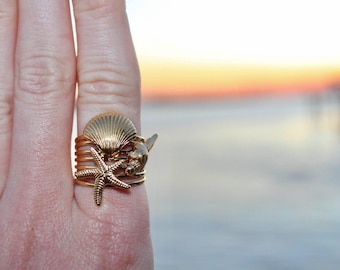 May include: A gold ring with a seashell and starfish design. The ring is stacked with other gold bands.