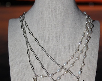 May include: Three necklaces displayed on a mannequin. The necklaces feature silver chains, pearls, and shark tooth pendants. The background shows an orange and yellow sunset over the water.