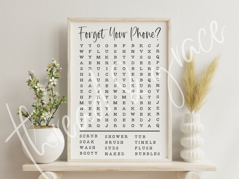 Puede incluir: Una impresi&oacute;n enmarcada con el texto "Forgot Your Phone?" y un crucigrama con las palabras "Scrub, Soak, Wash, Booty, Shower, Brush, Suds, Naked, Tub, Tinkle, Flush, Bubbles" enumeradas debajo. La impresi&oacute;n se muestra en un estante con un jarr&oacute;n blanco y una planta en maceta.