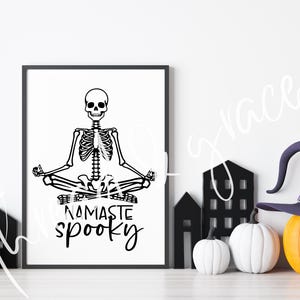 May include: A black and white printable design featuring a skeleton in a yoga pose with the text "Namaste Spooky".
