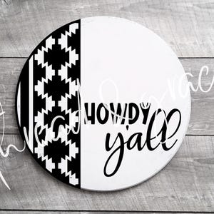 May include: A round wooden sign with a half-and-half design. One side features a black and white geometric pattern, while the other is white with the words "Howdy Y'all" in black script. The sign is a decorative item.