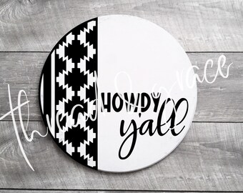 Puede incluir: Un letrero redondo de madera con un diseño dividido. Un lado presenta un patrón geométrico en blanco y negro, el otro es blanco con las palabras "Howdy Y'all" en escritura negra. Un artículo decorativo.
