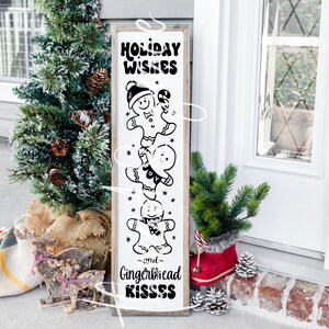 May include: A white wooden sign with black text and illustrations of gingerbread people. The sign reads "Holiday Wishes and Gingerbread Kisses".