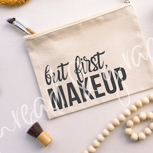 May include: A white canvas makeup bag with a black zipper and the text "but first, makeup" printed on the front.