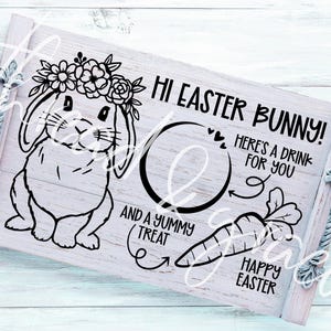 Puede incluir: Una bandeja de madera blanca con una ilustración en blanco y negro de un conejo de Pascua con una corona de flores. El texto "Hi Easter Bunny! Here's a drink for you and a yummy treat" está escrito en la bandeja. Las palabras "Happy Easter" también están escritas en la bandeja.