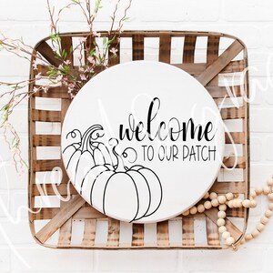 May include: A white round wooden sign with black text that reads "Welcome to our patch" and a black line drawing of pumpkins.