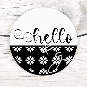 Puede incluir: Un diseño redondo de dos tonos con la palabra "hello" en elegante escritura negra. La mitad superior es blanca, mientras que la mitad inferior presenta un patrón floral negro. El diseño está sobre una superficie de madera.