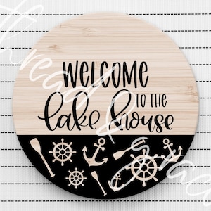May include: Round wooden sign with the text "Welcome to the Lake House" in black lettering. The bottom half of the sign is black with white nautical themed graphics including anchors, oars, and steering wheels.