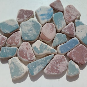 Könnte beinhalten: Eine Sammlung von 18 kleinen, unregelmäßig geformten Keramikfliesen in Blautönen, Rosa und Weiß. Die Fliesen haben eine gesprenkelte, marmorierte Optik.