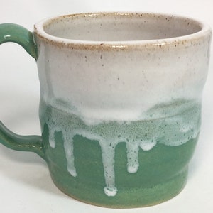Può includere: Tazza in ceramica fatta a mano con manico e base verdi, che sfuma nel bianco con un effetto smalto a goccia. Il bordo ha una finitura naturale macchiettata. Una tazza da caffè o tè artigianale unica.