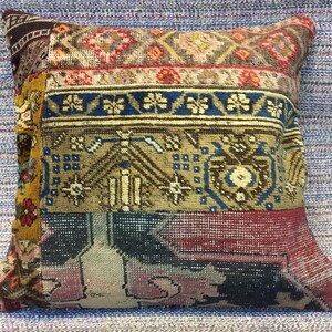 May include: A square patchwork cushion with sections of patterned fabric. The cushion features burgundy, gold, blue, and tan colours. The design incorporates geometric and floral motifs, creating a vintage aesthetic.
