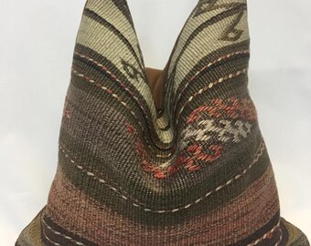 May include: A brown, red, and white patterned pillow with a geometric design. The pillow is made of woven fabric and has a brown leather trim.