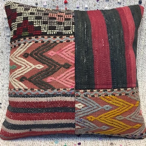 Puede incluir: Una funda de cojín de patchwork colorida con un patrón geométrico. La funda está hecha de tejido tejido y presenta una variedad de colores, incluyendo rojo, negro, rosa y amarillo.