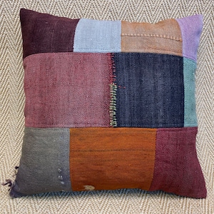 May include: A patchwork pillow with a variety of colors and textures, including burgundy, blue, brown, and orange. The pillow is made of different fabrics, including corduroy and linen.