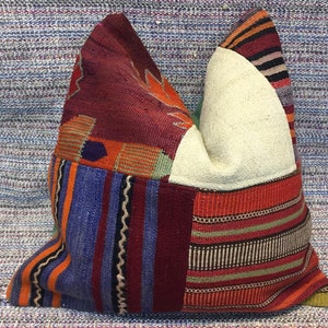 Puede incluir: Un cojín patchwork con una variedad de colores y patrones. El cojín presenta secciones de tela burdeos, naranja, azul y crema. El diseño incluye rayas, formas geométricas y motivos florales, creando una apariencia única y texturizada.