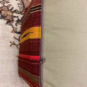 May include: A rectangular pillow with a patterned side and a solid side. The patterned side features horizontal stripes in shades of red, yellow, and brown. The solid side is a light green color. A zipper runs along the edge.