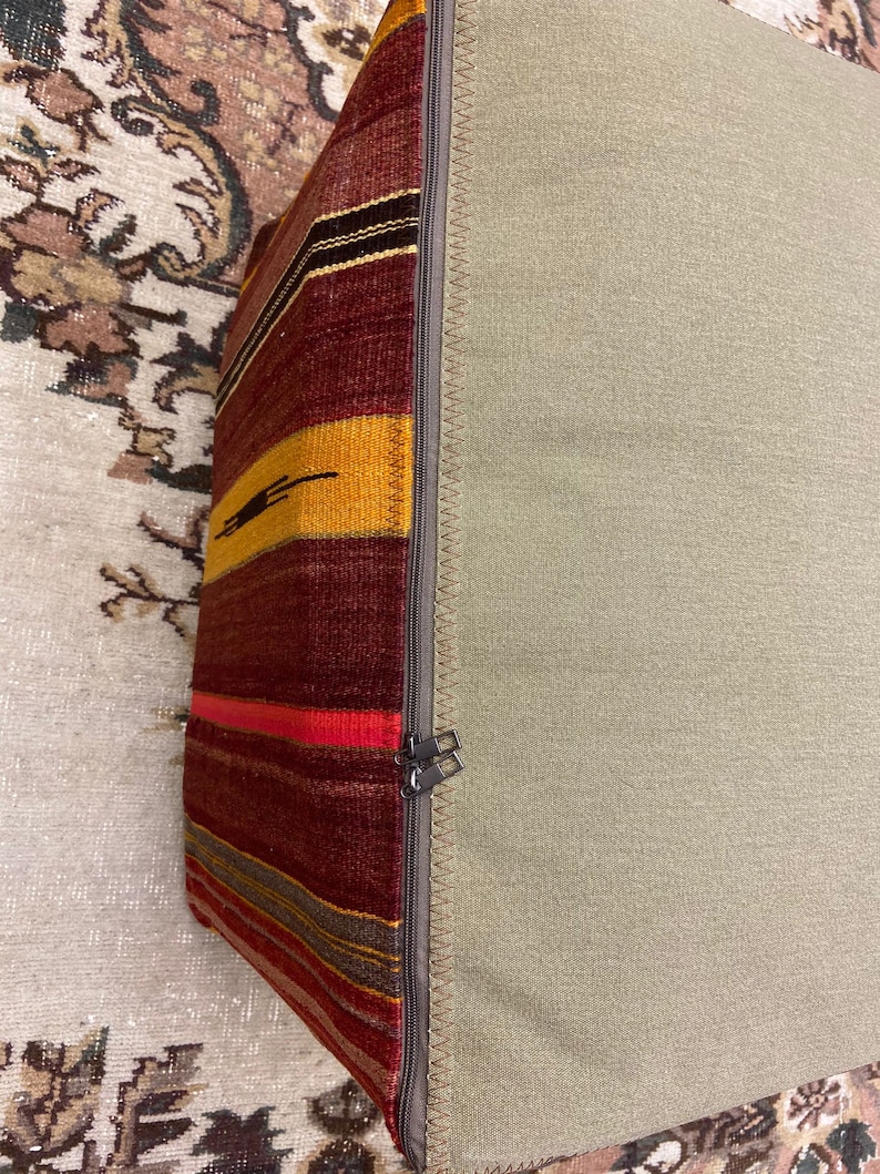 May include: A rectangular pillow with a patterned side and a solid side. The patterned side features horizontal stripes in shades of red, yellow, and brown. The solid side is a light green color. A zipper runs along the edge.
