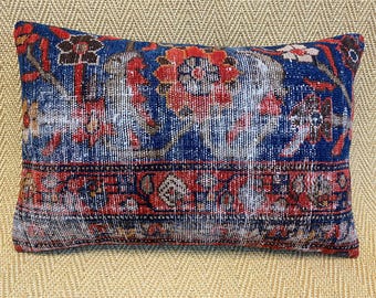 Puede incluir: Una almohada de tiro azul y roja con un patrón descolorido de aspecto vintage. La almohada está hecha de un tejido suave y tejido y tiene un borde con flecos.