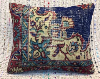 Puede incluir: Una almohada decorativa con un diseño estampado en azul, rojo y crema. La almohada está hecha de tela tejida y tiene un borde con flecos.