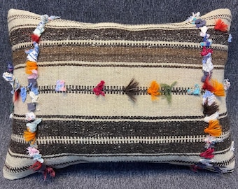May include: A striped throw pillow with brown and white stripes and colorful fabric tassels on the edges.